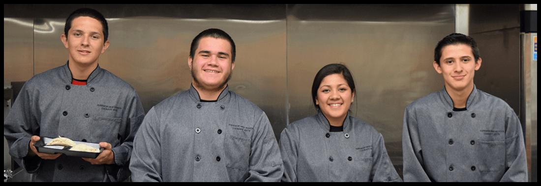 Students in chef uniforms pose together in a kitchen